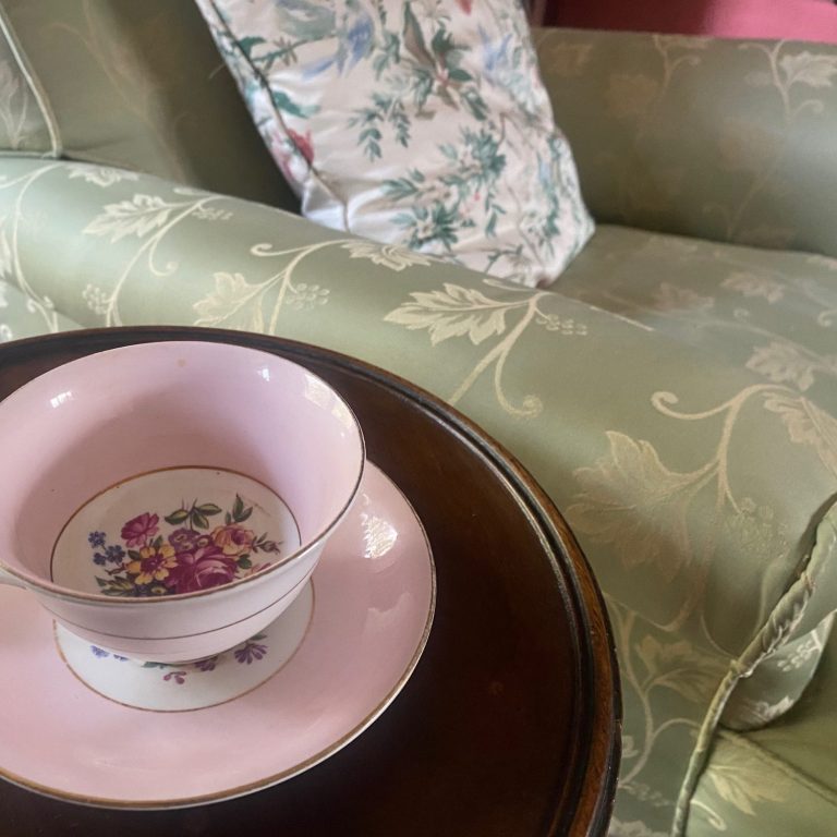 Tea cup and saucer beside green armchair. Pretty antique tea cup and saucer on a small table beside an elegant green satin covered antique armchair.
